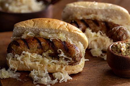 Brats on gourmet buns topped with sauerkraut and mustard for tailgate parties catered by Collective Brands Catering.