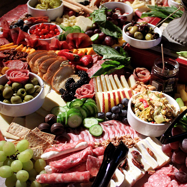 Spread of appetizers on custom made charcuterie board with fruits, vegetables, breads, sliced meats and more from Pennsylvania wedding and corporate event caterer Collective Brands Catering.