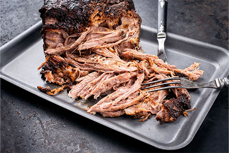 Shredded pulled pork on a tray with two forks, ready to be served.